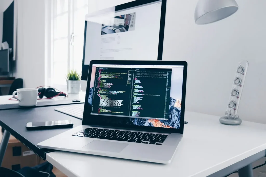 Schreibtisch mit MacBook und Programmcode: Häufige Fragen zur Website-Wartung in Ulm